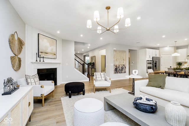 living area featuring recessed lighting, a glass covered fireplace, a chandelier, light wood-type flooring, and stairs