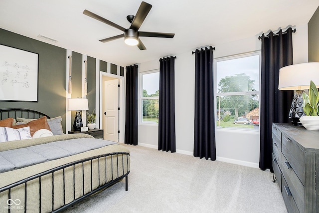 carpeted bedroom featuring a ceiling fan, multiple windows, visible vents, and baseboards