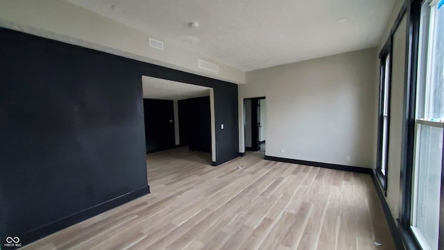 empty room featuring light wood-style flooring, visible vents, and baseboards