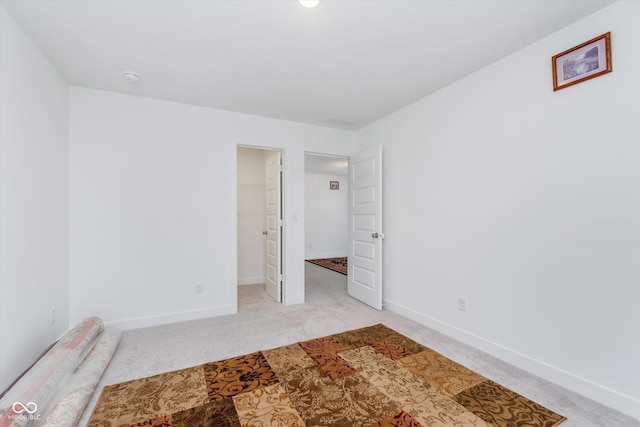unfurnished bedroom featuring a walk in closet, baseboards, and light colored carpet