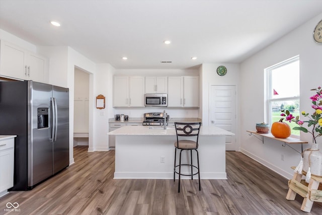 kitchen with white cabinets, stainless steel appliances, wood finished floors, and a kitchen island with sink
