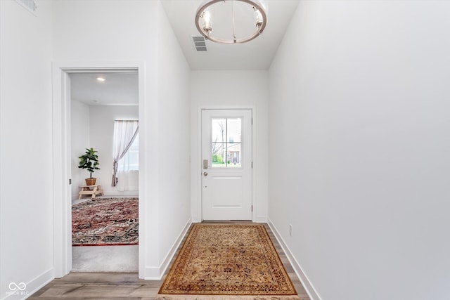 doorway to outside with an inviting chandelier, light wood finished floors, visible vents, and baseboards