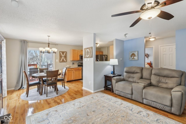 living area featuring light wood-style floors, a textured ceiling, baseboards, and ceiling fan with notable chandelier