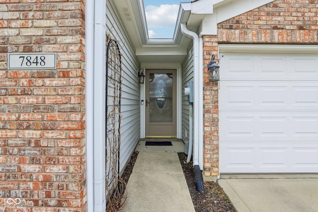 doorway to property featuring a garage and brick siding