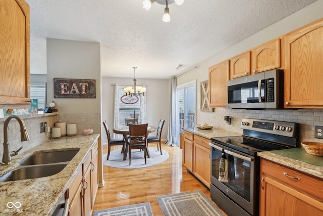 kitchen with light wood-style flooring, a sink, light stone countertops, stainless steel appliances, and a notable chandelier