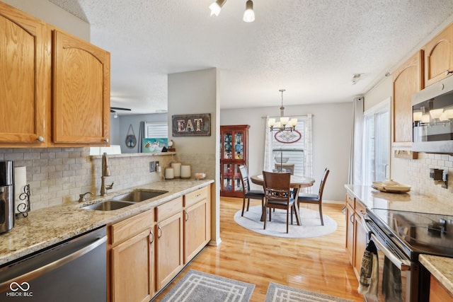 kitchen with light wood finished floors, a sink, light stone countertops, stainless steel appliances, and a notable chandelier