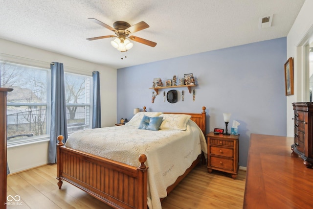 bedroom with visible vents, ceiling fan, light wood-style flooring, and a textured ceiling