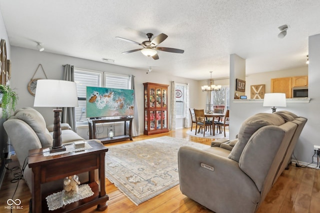 living area with light wood-type flooring, a textured ceiling, and ceiling fan with notable chandelier