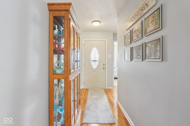 doorway featuring light wood-style floors, baseboards, and a textured ceiling