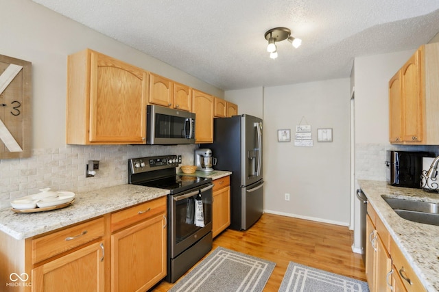 kitchen featuring light stone counters, a sink, stainless steel appliances, light wood-type flooring, and backsplash