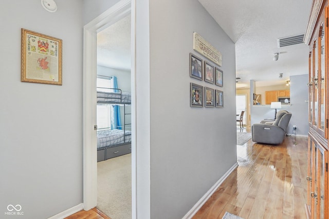 hall with a textured ceiling, baseboards, visible vents, and light wood-style floors