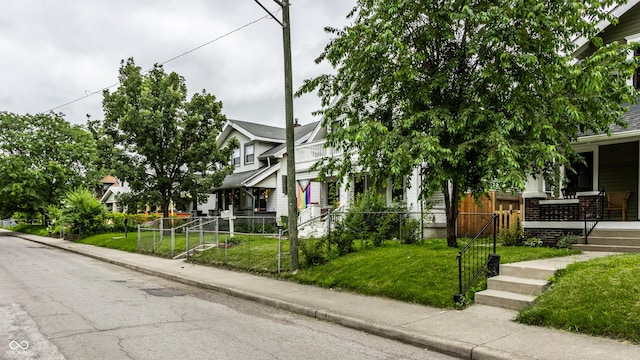 view of property hidden behind natural elements featuring covered porch, fence, and a front lawn