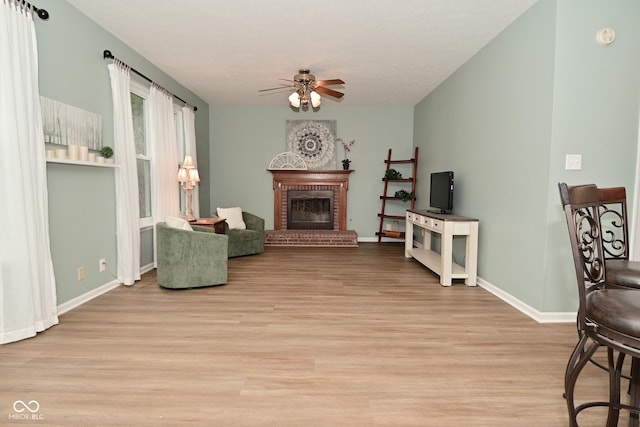 living area with light wood-type flooring, a brick fireplace, ceiling fan, and baseboards