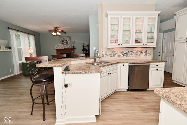 kitchen with light wood-style flooring, a sink, ceiling fan, light stone countertops, and a kitchen bar