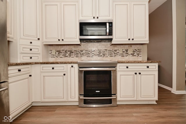 kitchen featuring light wood-style flooring, stainless steel appliances, baseboards, cream cabinetry, and tasteful backsplash