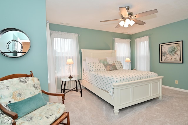 bedroom with light carpet, ceiling fan, multiple windows, and baseboards