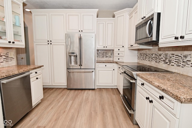 kitchen featuring appliances with stainless steel finishes, white cabinetry, light wood-style floors, and glass insert cabinets