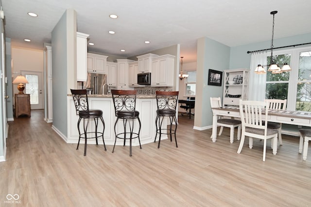 kitchen featuring light wood-style floors, appliances with stainless steel finishes, a breakfast bar, and a chandelier