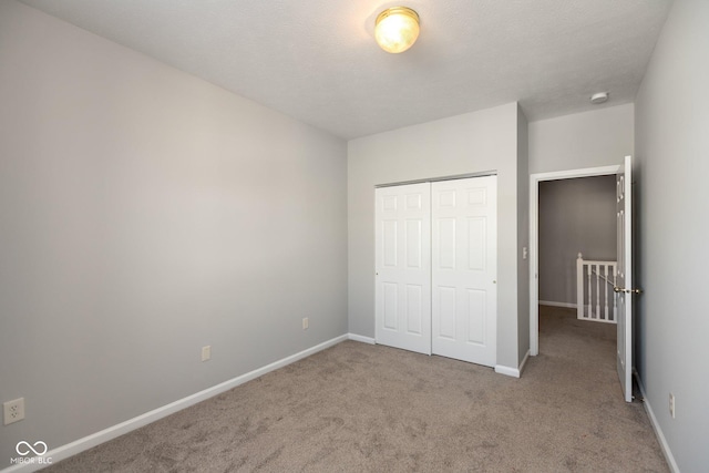 unfurnished bedroom with a textured ceiling, carpet floors, a closet, and baseboards