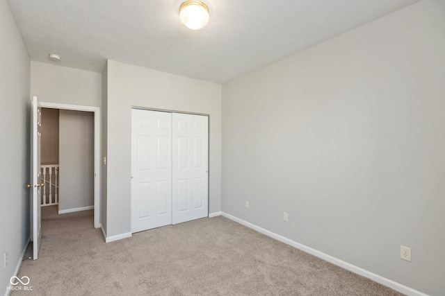 unfurnished bedroom with light carpet, a textured ceiling, baseboards, and a closet