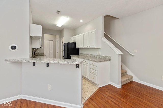 kitchen with light stone counters, a breakfast bar, freestanding refrigerator, white cabinetry, and a peninsula