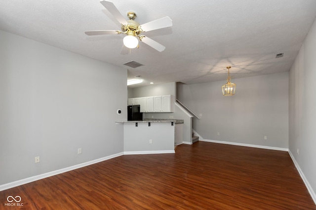 unfurnished living room with dark wood-style floors, visible vents, stairway, baseboards, and ceiling fan with notable chandelier