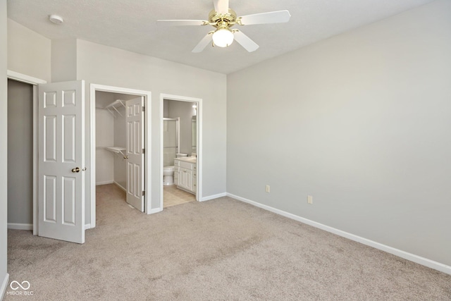 unfurnished bedroom with connected bathroom, light carpet, baseboards, a closet, and a walk in closet