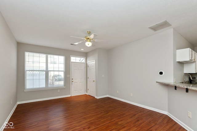 unfurnished living room featuring a sink, a ceiling fan, visible vents, baseboards, and dark wood finished floors