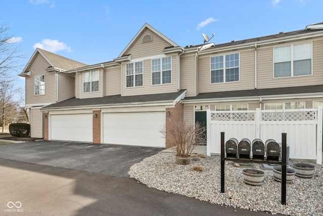 multi unit property featuring a garage, brick siding, driveway, and fence