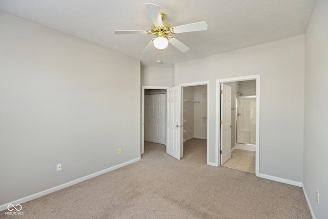 unfurnished bedroom with light carpet, baseboards, a walk in closet, and ensuite bathroom