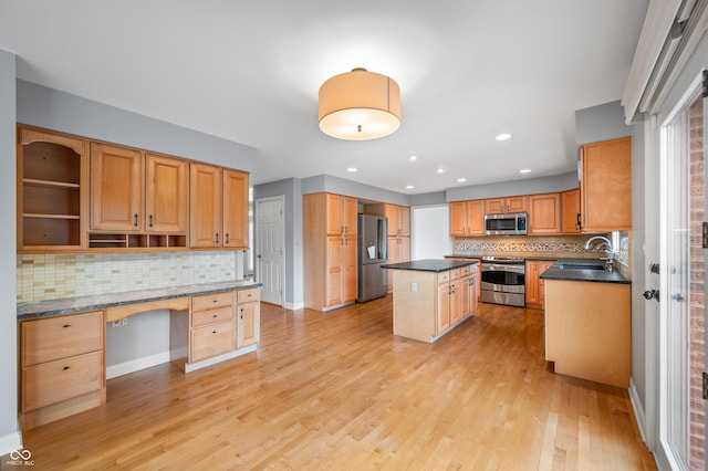 kitchen with stainless steel appliances, built in study area, a sink, a kitchen island, and light wood-type flooring