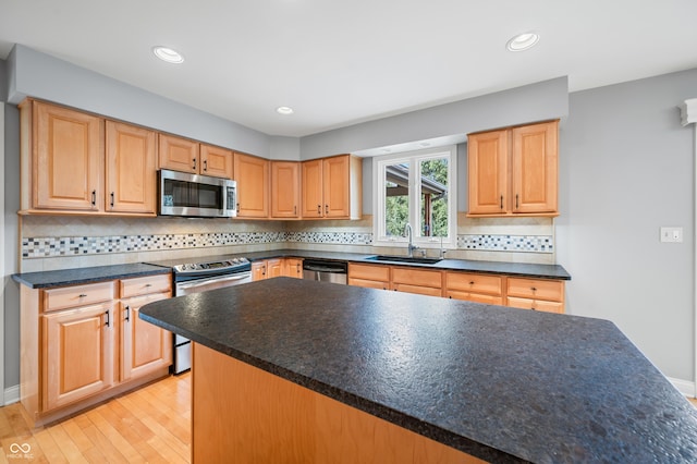 kitchen featuring decorative backsplash, dark countertops, appliances with stainless steel finishes, light wood-type flooring, and a sink