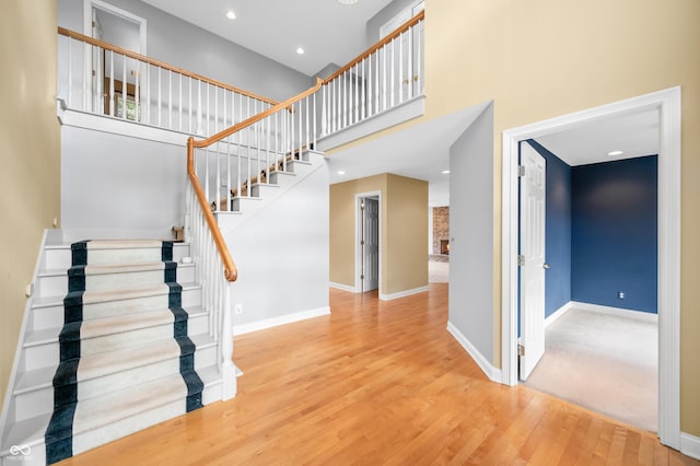 stairway with recessed lighting, wood finished floors, a towering ceiling, and baseboards