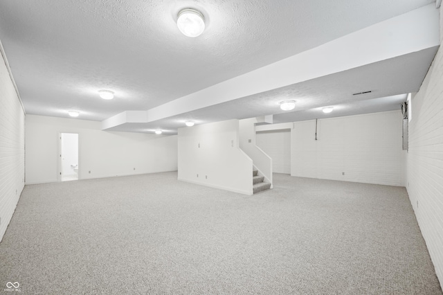 finished basement with a textured ceiling, brick wall, stairway, and light colored carpet