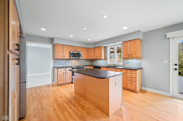 kitchen with stainless steel appliances, a sink, light wood finished floors, dark countertops, and tasteful backsplash