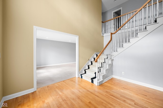 stairway with a towering ceiling, baseboards, and wood finished floors