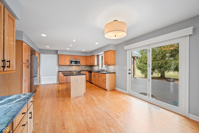 kitchen with light wood finished floors, stainless steel appliances, dark countertops, visible vents, and backsplash