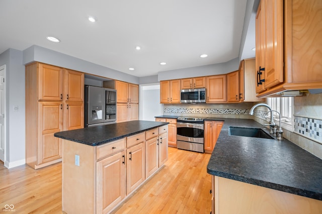 kitchen featuring dark countertops, a kitchen island, stainless steel appliances, light wood-style floors, and a sink