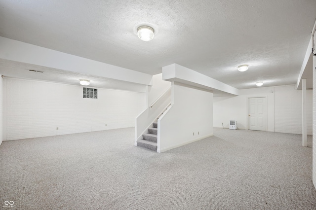 finished basement featuring carpet, visible vents, stairway, a textured ceiling, and brick wall