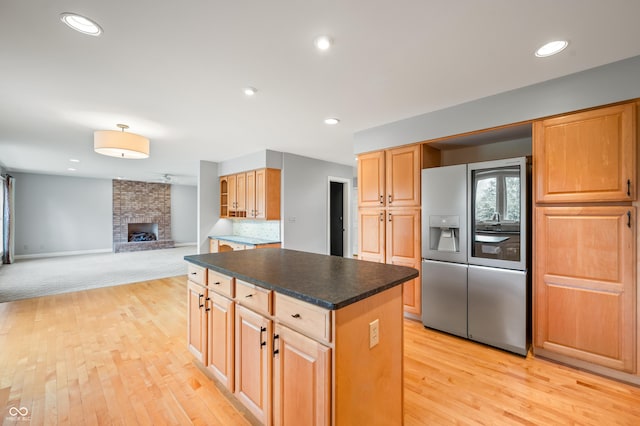 kitchen with a fireplace, a kitchen island, light wood-type flooring, dark countertops, and stainless steel fridge