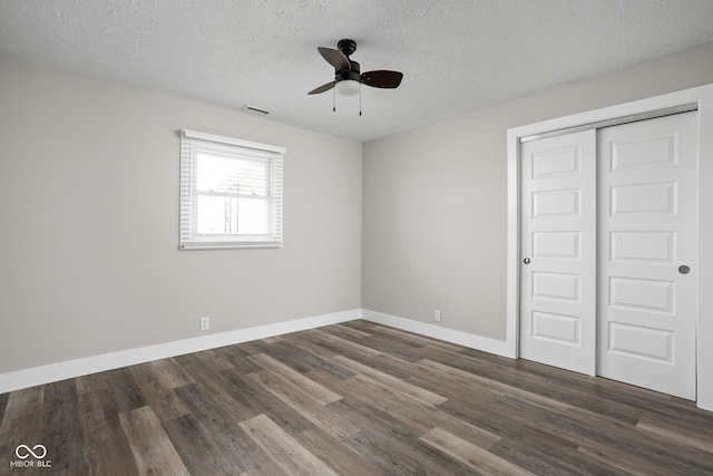 unfurnished bedroom with a textured ceiling, visible vents, baseboards, a closet, and dark wood-style floors