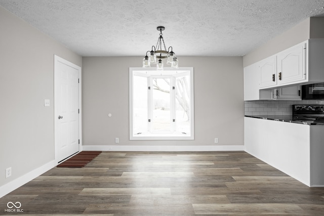 unfurnished dining area with dark wood-type flooring, a textured ceiling, baseboards, and an inviting chandelier