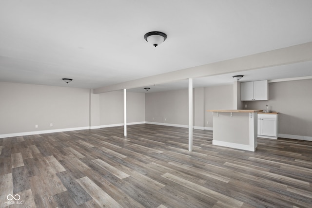 finished below grade area featuring wet bar, dark wood-style flooring, a sink, and baseboards