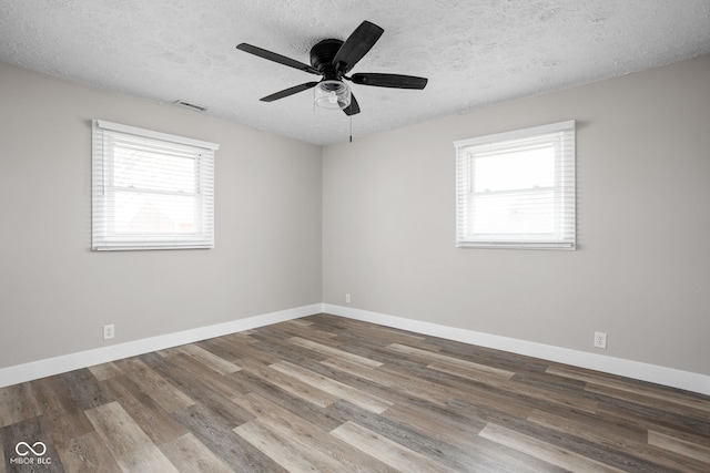 empty room with a wealth of natural light, visible vents, baseboards, and wood finished floors