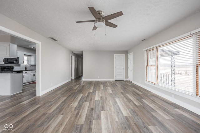 unfurnished living room with a sink, wood finished floors, visible vents, and baseboards