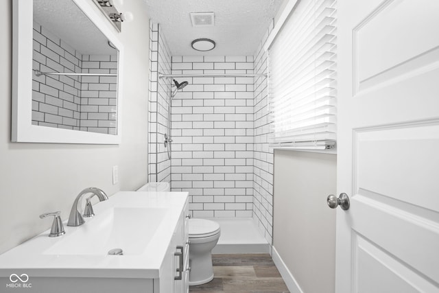 bathroom with tiled shower, a textured ceiling, toilet, and vanity