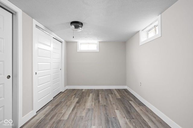 basement featuring a textured ceiling, wood finished floors, and baseboards