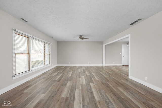 spare room featuring ceiling fan, a textured ceiling, wood finished floors, visible vents, and baseboards