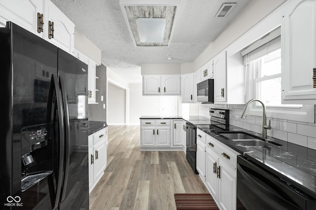 kitchen with black appliances, light wood finished floors, a sink, and white cabinetry