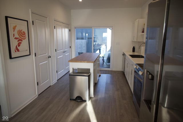 kitchen with a sink, wood counters, dark wood-style floors, appliances with stainless steel finishes, and white cabinets